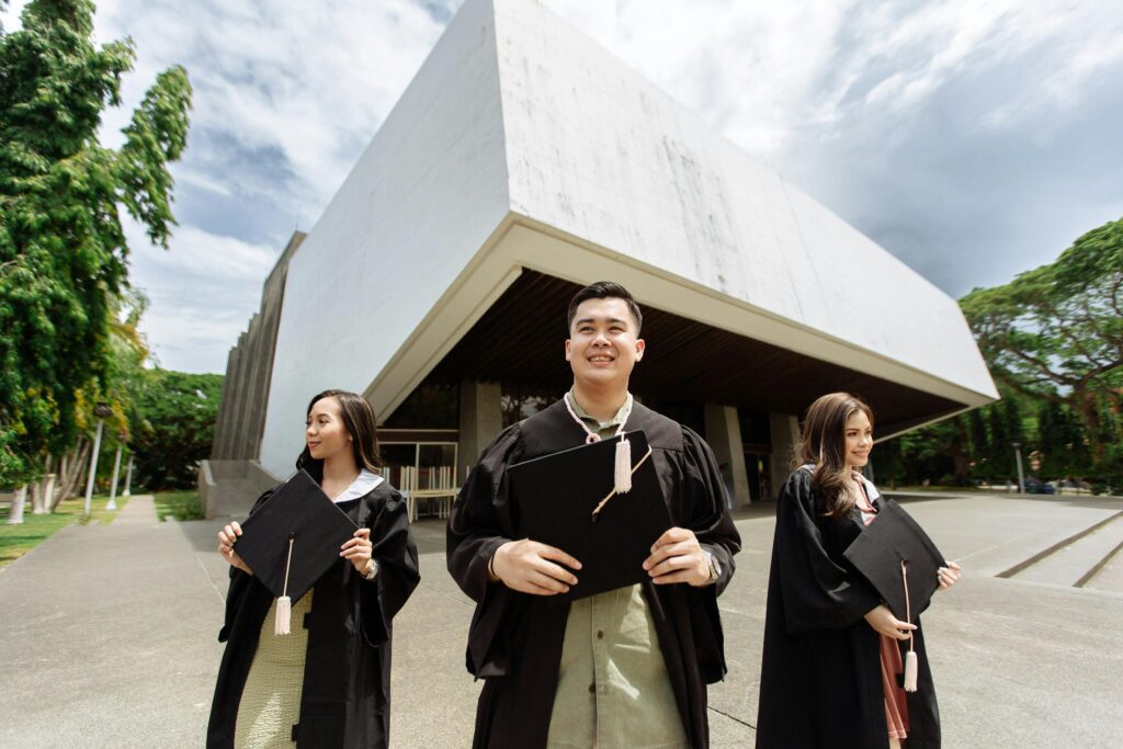 Three graduates celebrating outside a contemporary building with diplomas in hand.